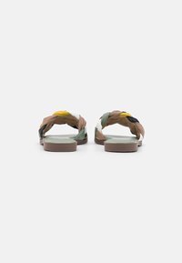 Sandalias de verano trenzadas que presentan una mezcla de materiales en verde, amarillo, blanco y marrón. Suela plana con un acabado texturizado.