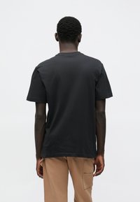 Tricou negru din bumbac, cu decolteu clasic rotund și mâneci scurte, având un croi lejer și fără modele sau grafice vizibile.