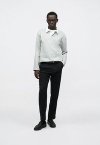 Grå långärmad pikétröja med vit krage, kombinerad med svarta smala byxor och svarta skor. Mjukt tyg och minimalistisk design.