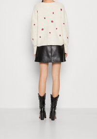 Krämfärgad stickad tröja med rosa blommig brodyr, kombinerad med en svart läder mini kjol och svarta klackiga cowboystövlar.