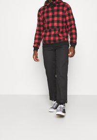 Rot-schwarz kariertes Flanell-Hoodie mit Kängurutasche, kombiniert mit schwarzen Hosen und schwarz-weißen Sneakers.