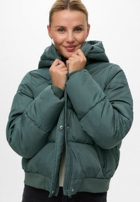 Zelena jakna od puf materijala s kapuljačom, quatirana tekstura, prednji zip i rebraste manžete. Ima ležeran kroj i odvojivu kapuljaču.