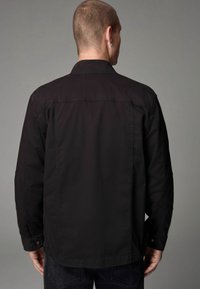Zwarte shirt met een kraag, lange mouwen en zichtbare stiksels op de achterkant, gecombineerd met donkere jeans.
