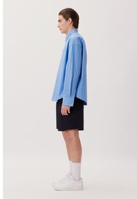 Camicia azzurra a righe con abbottonatura, dal taglio rilassato, abbinata a pantaloni corti neri. Indossata con sneaker bianche e calzini alla caviglia.