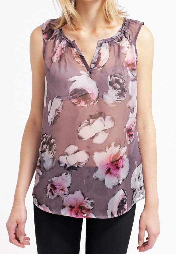Top trasparente viola con un motivo floreale in rosa e bianco. Presenta un colletto arricciato e una vestibilità comoda. Abbinato a pantaloni neri.