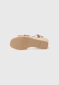 Brown wedge sandal with a textured sole, featuring dual straps and a buckle detail. The sole is made of a tan, rubber-like material.