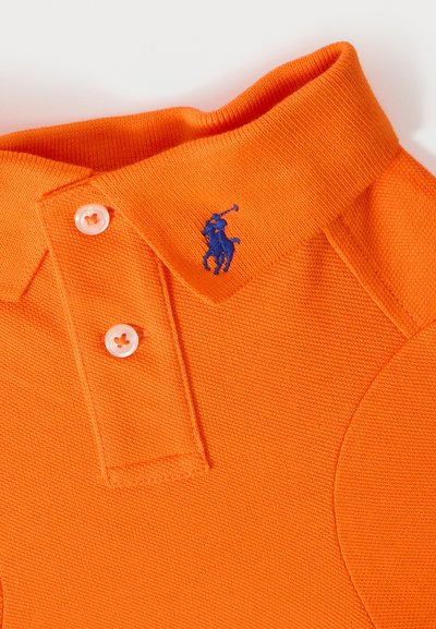 Col de polo orange avec deux boutons blancs et un petit logo bleu brodé représentant un cheval et un cavalier tenant une maille de polo.