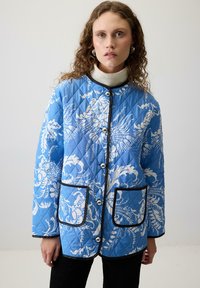 Plavi jakna sa kreiranim uzorkom, bijelim cvjetnim uzorcima, crnim detaljima i srebrnim gumbima. Ima dva prednja džepa i okrugli izrez.