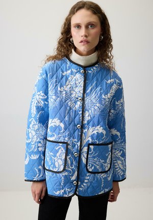 Quilted blå jakke med hvidt blomstermønster, sort kant og sølvknapper. Har to forlommer og en rund halsudskæring.