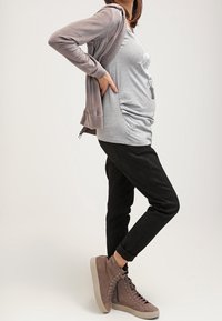 Sudadera gris sobre una camiseta gráfica gris, pantalones negros ajustados y zapatillas altas de color marrón claro con cordones y cremalleras laterales.