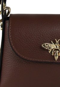 Bruine leren handtas met textuur en een afgeronde klep, voorzien van een gouden bijembleem en een zwarte kettingband.