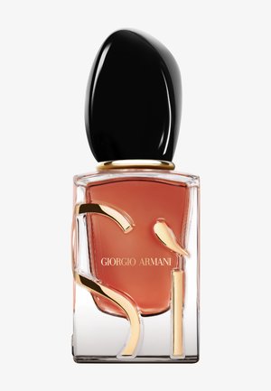 Szklana butelka perfum z przezroczystą podstawą, pomarańczowym płynem, czarną owalną zakrętką i złotymi akcentami z napisem "Giorgio Armani."