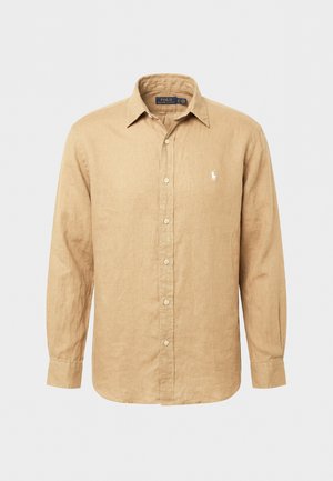 Béžinė ilgomis rankovėmis marškiniai su sagomis ir išskleistu apykakle, ant kairiojo krūtinės krašto išsiuvinėtas Polo Ralph Lauren prekės ženklo logotipas.