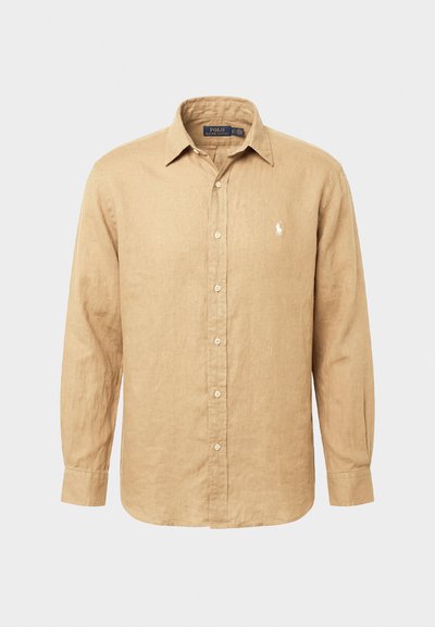 Béžinė ilgomis rankovėmis marškiniai su sagomis ir išskleistu apykakle, ant kairiojo krūtinės krašto išsiuvinėtas Polo Ralph Lauren prekės ženklo logotipas.