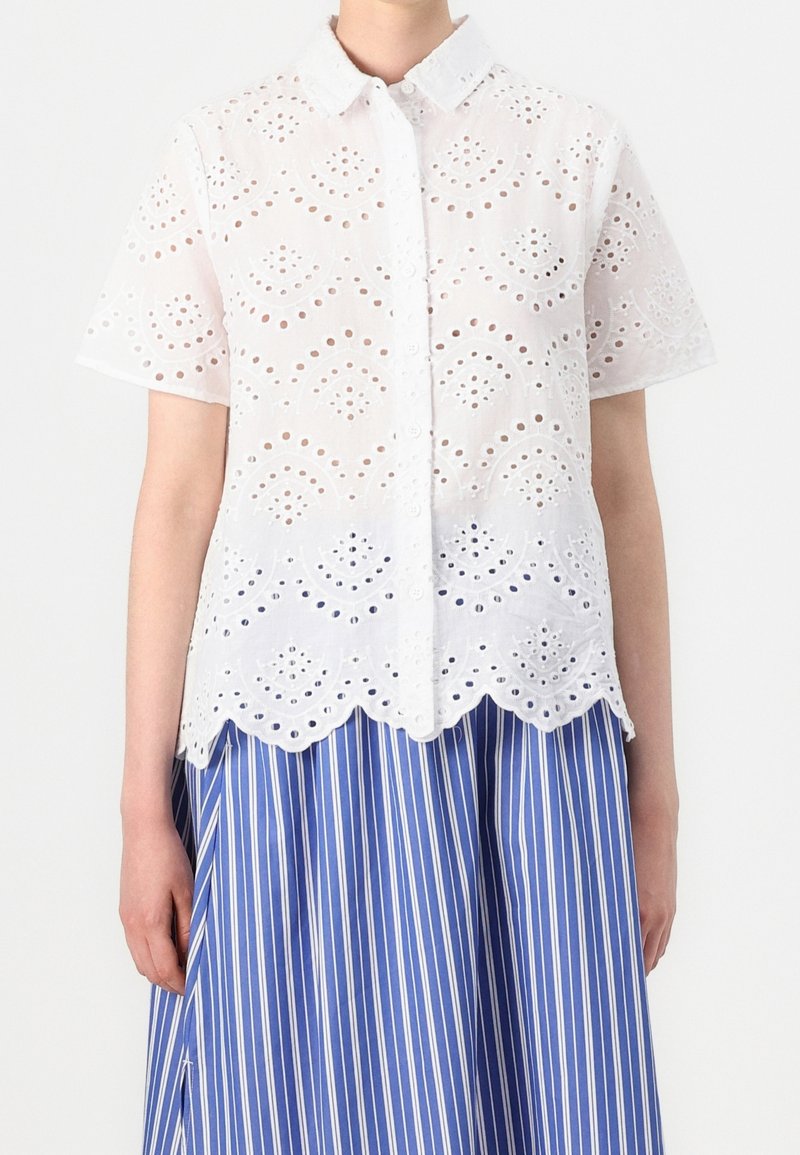 Woman wearing a white short-sleeve button-up eyelet blouse paired with a blue and white vertical striped skirt.