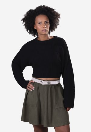 Sort ribbet cropped sweater med lange ærmer, parret med en mørkegrøn nederdel med sidelommer og et lyst bælte i taljen.