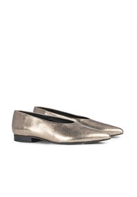 Zapatos planos metálicos dorados con diseño de punta, textura suave y tacón bajo negro. Presentan un sutil acento de logo en el lateral.
