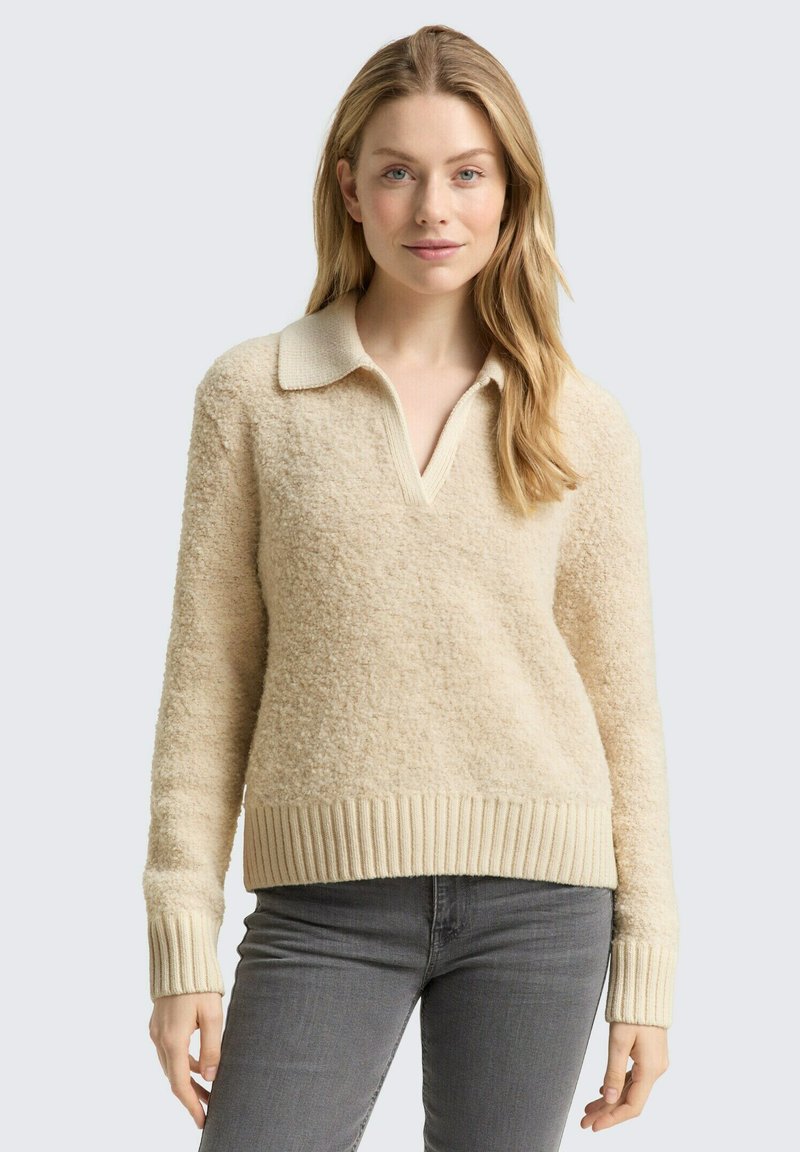 Kremowy sweter typu pulower wykonany z teksturowanego materiału, z kołnierzykiem oraz ściągaczami przy rękawach i u dołu.