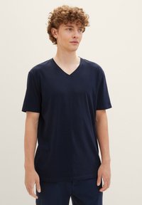 Tricou din bumbac bleu marin cu decolteu în V, mâneci scurte, croi lejer, textură fină și design minimalist. Fără modele sau accente vizibile.