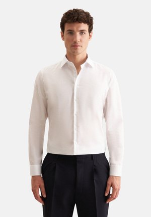 Witte lange mouwen shirt met een puntige kraag en knopen aan de voorkant, gemaakt van een gladde, lichte stof, gedragen met zwarte broeken.