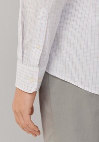 Camicia a maniche lunghe a scacchi bianca, con motivi a griglia rossi e blu, polsi con bottoni e una texture in cotone liscia.