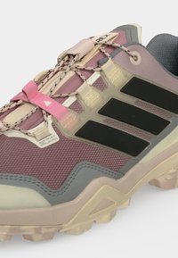 Μωβ και μπεζ αθλητικό παπούτσι Adidas με μαύρες ρίγες, ροζ θηλιά κορδονιού και μοτίβο στα κορδόνια σε μια υφασμάτινη, ανθεκτική σόλα.