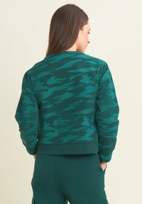 Felpa verde mimetica con colletto rotondo, tessuto texturizzato e polsini a costine. Il design presenta diverse tonalità di verde.