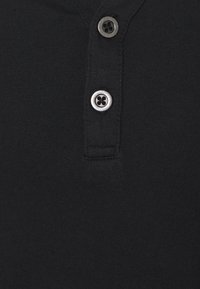 Polo negro con tejido texturizado, con un cierre de tres botones y un cuello de canalé, destacado por acentos de botones grises.