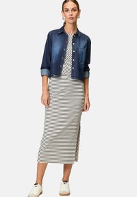 Denim jacket over a striped, knee-length dress in white and black. Sneakers with a light upper and tan sole. Model displays casual outfit.