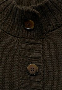 Brun stickad tröja med ribbad krage och två stora, mörka knappar framtill. Texturen är grov och tyget ser varmt ut.