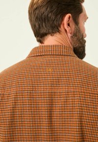 Braun kariertes Hemd mit kleinen Quadraten in Orange und Schwarz, ausgestattet mit einem Kragen, knöpfbarem Design und einem Logo-Patch auf der Rückseite.