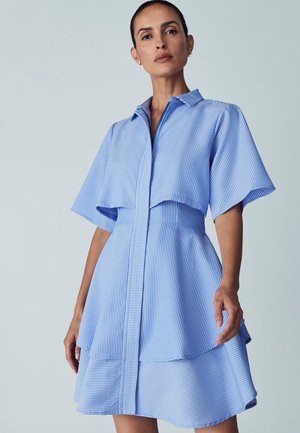 Robe chemise à rayures bleues et blanches avec des manches courtes évasées, un devant à boutons et une jupe à volants. Tissu lisse avec une coupe structurée.