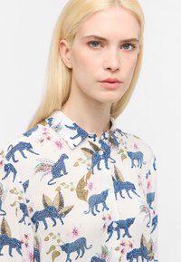 Witte shirt met blauwe panterprint, met een kraag en knoopsluiting. Bloemen- en bladaccenten in roze en groen. Soepele textuur.