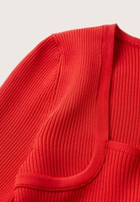 Primo piano di un tessuto a maglia rigata di un brillante rosso, che mostra le cuciture delle maniche e del collo, con un motivo verticale testurizzato.