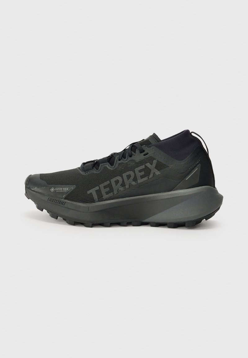 Chaussure de trail Adidas Terrex noire avec tige GORE-TEX, semelle épaisse et marquage "TERREX" sur le côté, présentée de profil sur fond gris.