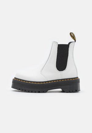 Hvid læder Chelsea-støvle med sort elastisk sidepanel, tyk sort sål, gul syning og mærket trækflig på neutral baggrund.