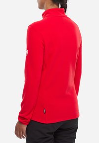 Pull rouge à manches longues avec un col montant, en tissu texturé, présentant un logo discret sur la manche gauche et un ourlet droit.