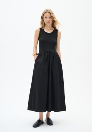 Robe noire sans manches avec un haut ajusté et une jupe évasée plissée. Fabriquée en tissu côtelé, elle dispose de poches latérales et d'une texture lisse.