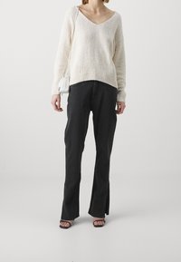 Crème, gebreide trui met een brede V-hals en geribde zoom; gecombineerd met zwarte, losse jeans met zijsplitten; zwarte, hoge sandalen.