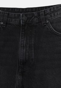 Sort denimjeans nærbillede, der viser det forreste linning, knaplukning, bæltestropper og detaljer ved den forreste lomme.