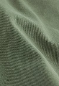 Vihreä kangas ribbikujulla, jossa on hienovaraisia taitoksia ja vaihtelevaa valonheijastusta, mikä viittaa keskikokoiseen materiaaliin.