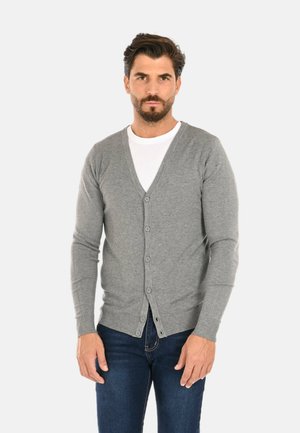 Cardigan grigio realizzato in materiali morbidi, con scollatura a V, chiusura a bottoni e polsini a coste. Abbinato a una t-shirt bianca e jeans scuri.