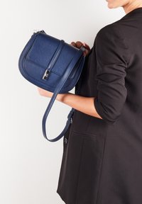 Granatowa skórzana torba na ramię o zorganizowanej formie, z płaską klapą z przodu i odczepianym paskiem; posiada zapięcie w kolorze srebrnym.