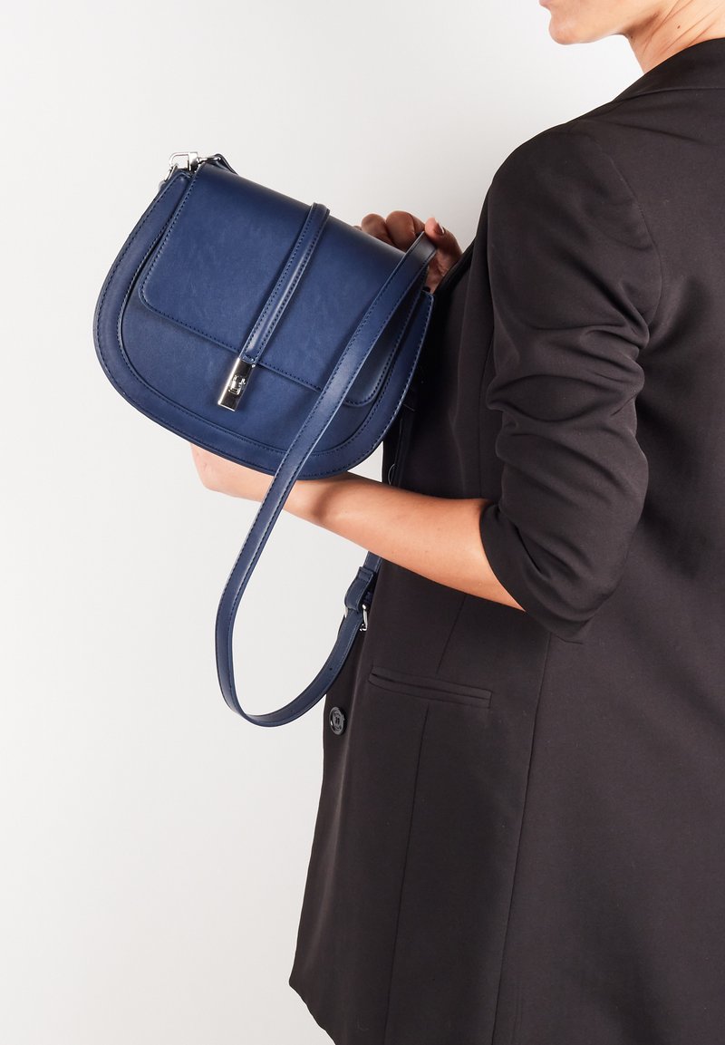 Granatowa skórzana torba na ramię o zorganizowanej formie, z płaską klapą z przodu i odczepianym paskiem; posiada zapięcie w kolorze srebrnym.