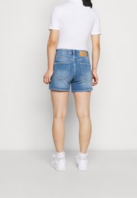 Džíny šortky ve světle modré barvě, s vysokým pasem, pěti kapsami a hnědou koženou nášivkou. Kombinované s přiléhavým bílým topem a bílými teniskami.