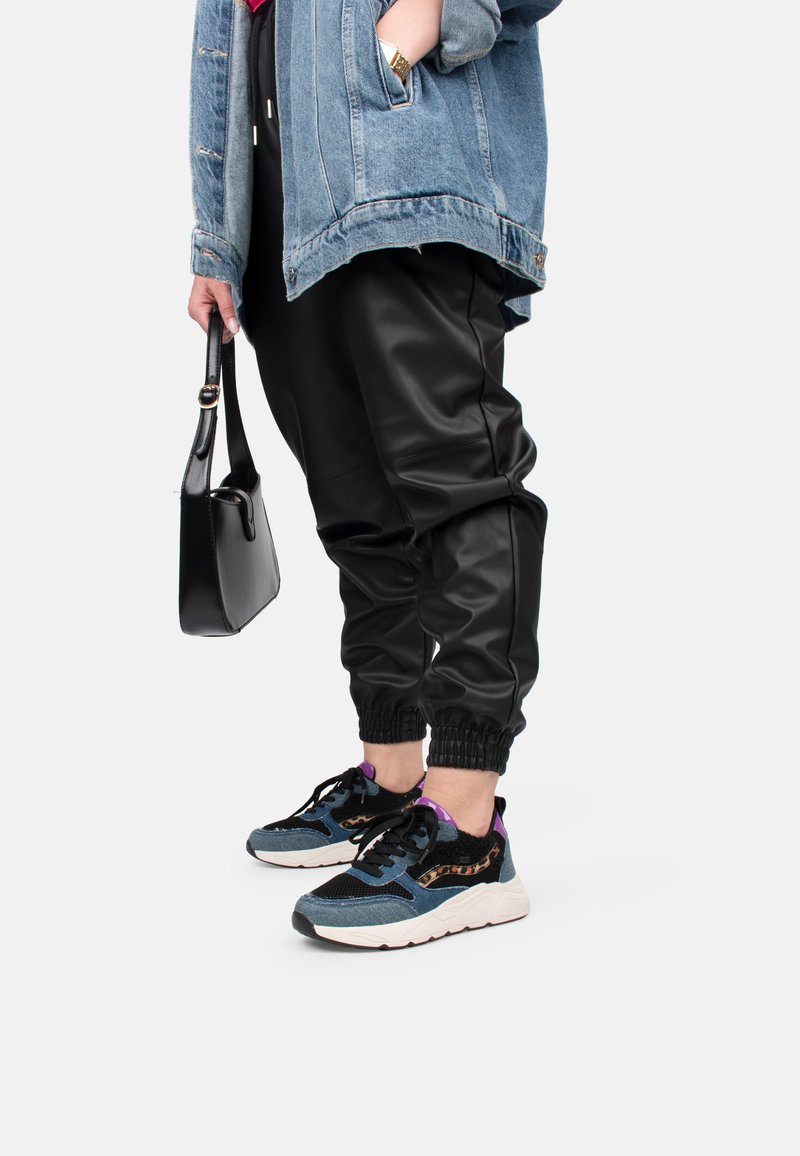 Jeansjacke, schwarze Jogginghosen aus Kunstleder mit elastischen Bündchen und mehrfarbige Sneakers mit strukturiertem Muster und kontrastierenden Akzenten.