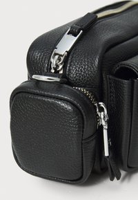 Geantă din piele neagră cu o suprafață texturată, compartimente cu fermoar și accente din metal argintiu. Compactă, cu un design structurat.