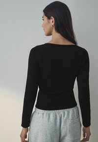 Zwarte langemouwen ribgebreide top met een vierkante halslijn, gecombineerd met lichtgrijze sweatpants met zijzakken en een relaxte pasvorm.