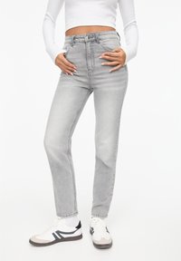 Jean gris taille haute avec une coupe droite, un effet délavé, un design à cinq poches et des détails de couture subtils. Associé à des baskets blanches.