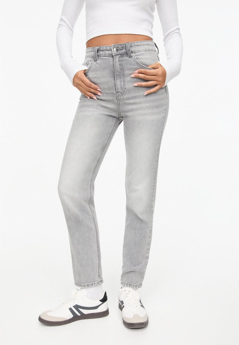 Jean gris taille haute avec une coupe droite, un effet délavé, un design à cinq poches et des détails de couture subtils. Associé à des baskets blanches.